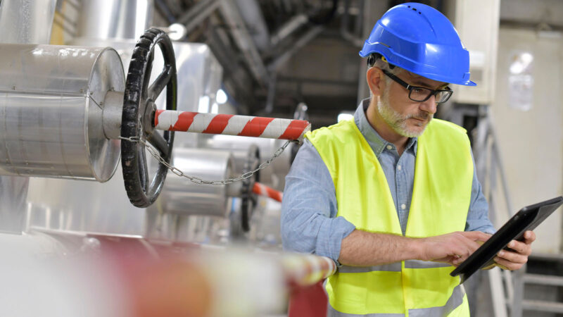 Agence développement solutions digitales homme dans une usine entouré de machines regardant sa tablette