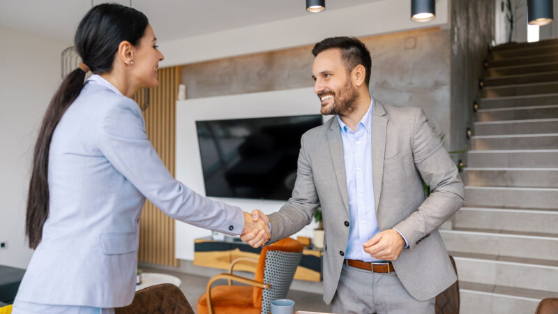 Agence développement solutions digitales femme serrant la main d'un homme, tous deux en costard dans une belle maison